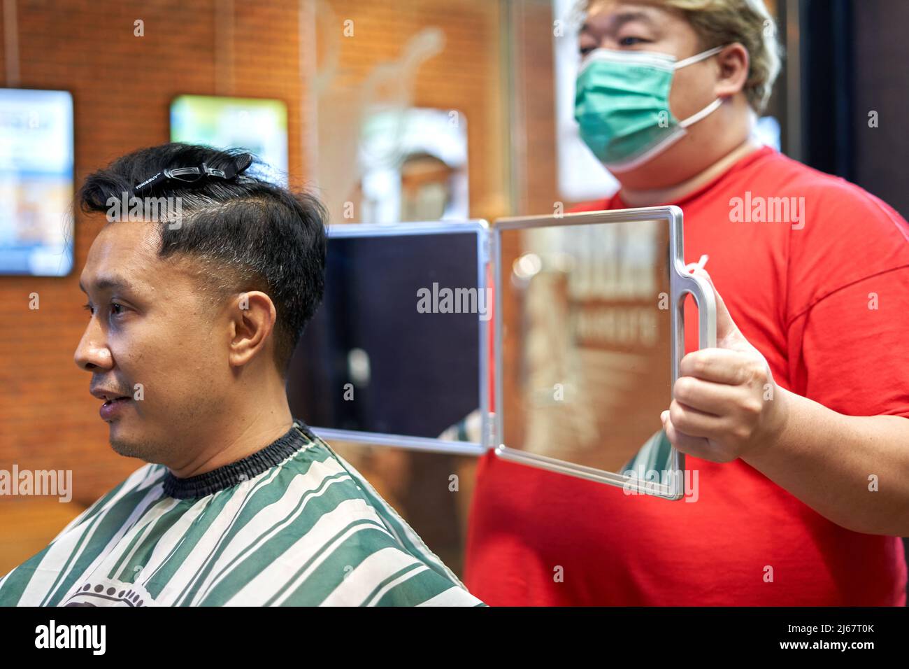 Barber with mask displaying the haircut to a client using a mirror Stock Photo