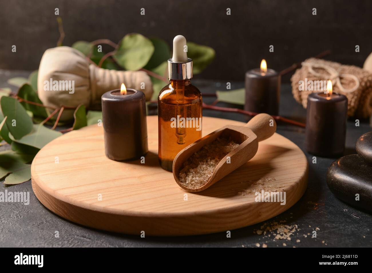 Wooden board with bottle of essential oil, burning candle and sea salt