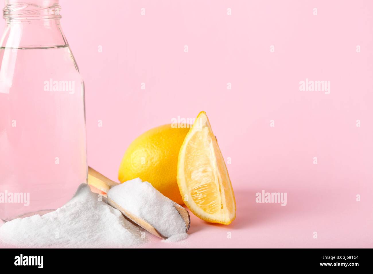 Scoop with baking soda, bottle of water and lemon on pink background