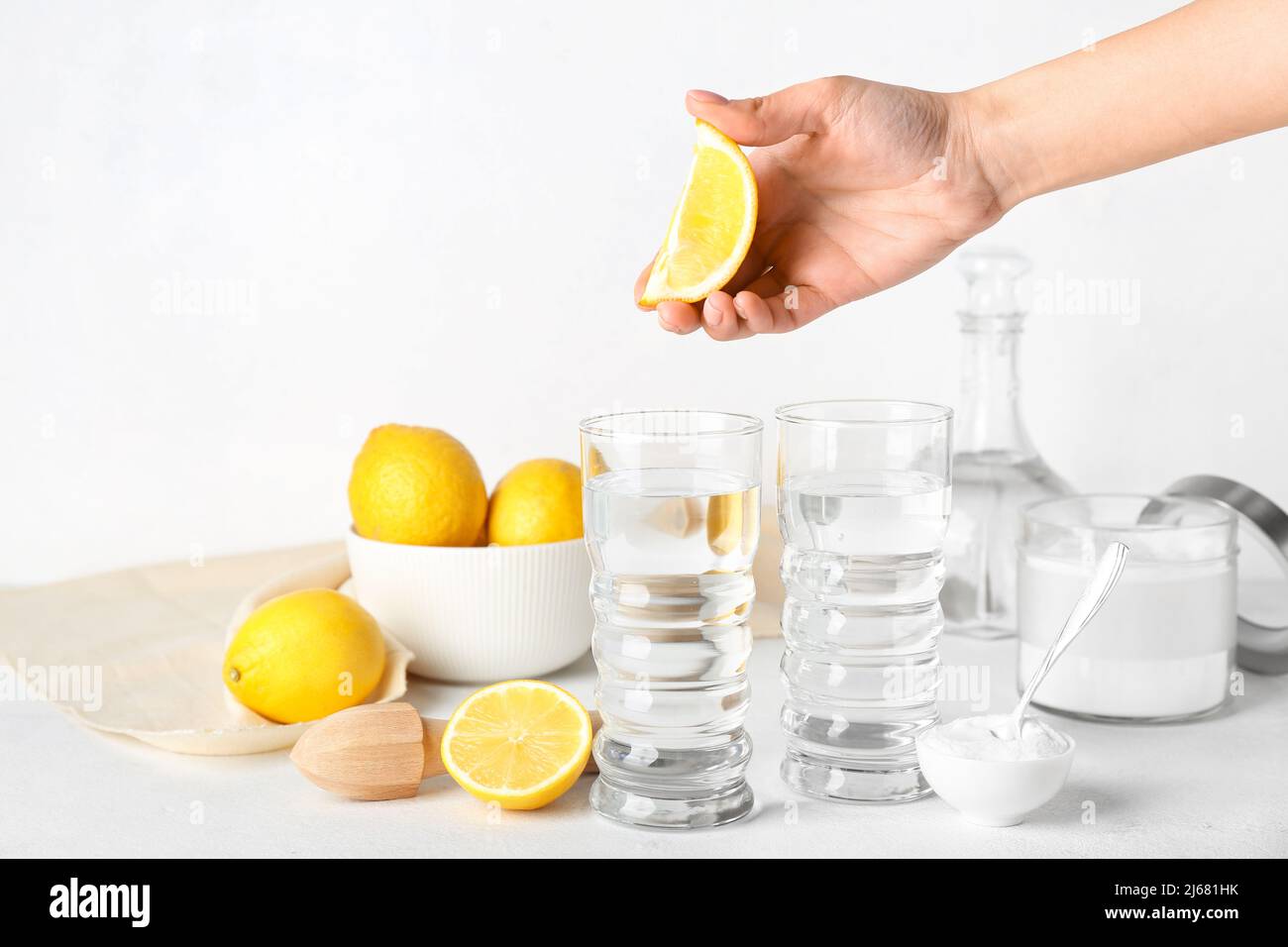 Female hand with lemon, glasses of water and baking soda on light