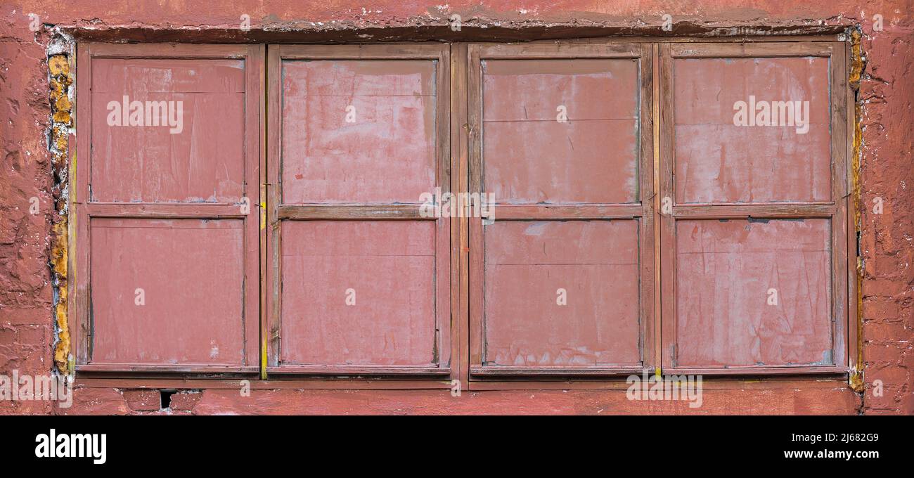 wood window with painted glass on red plaster wall. abandoned industrial building background. Stock Photo