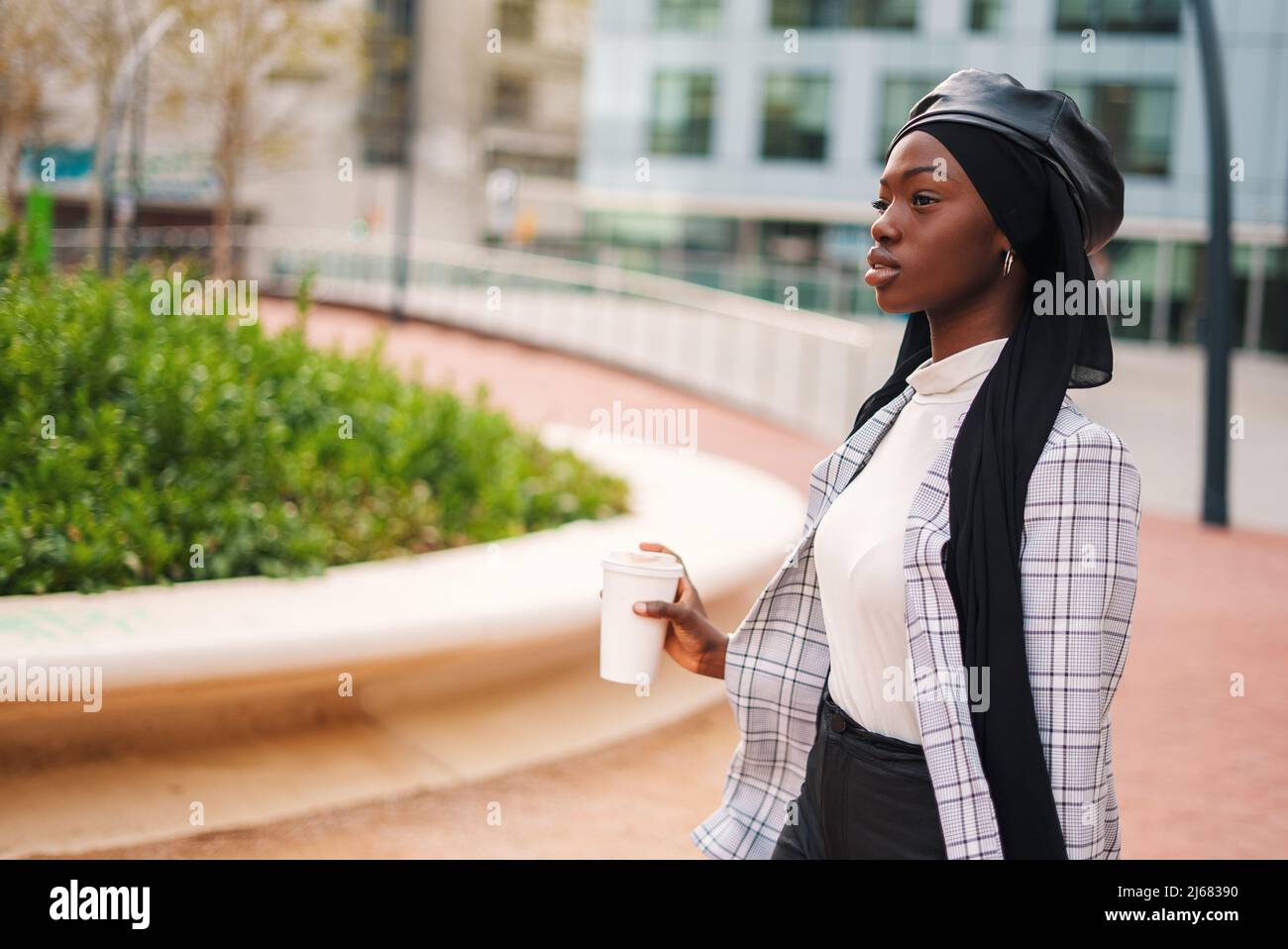 Black woman in headscarf with takeaway beverage in park Stock Photo
