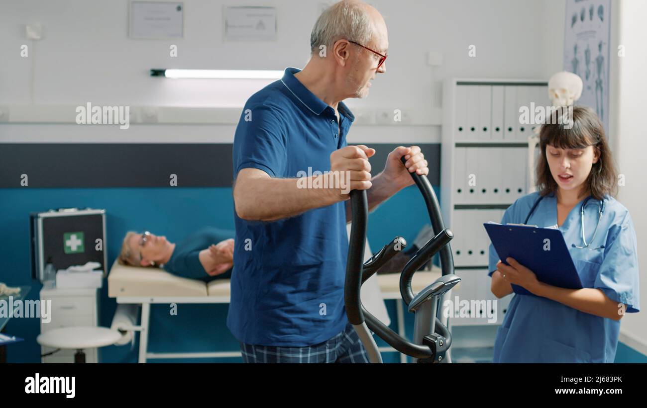 Medical nurse assisting elder patient doing physical exercise on