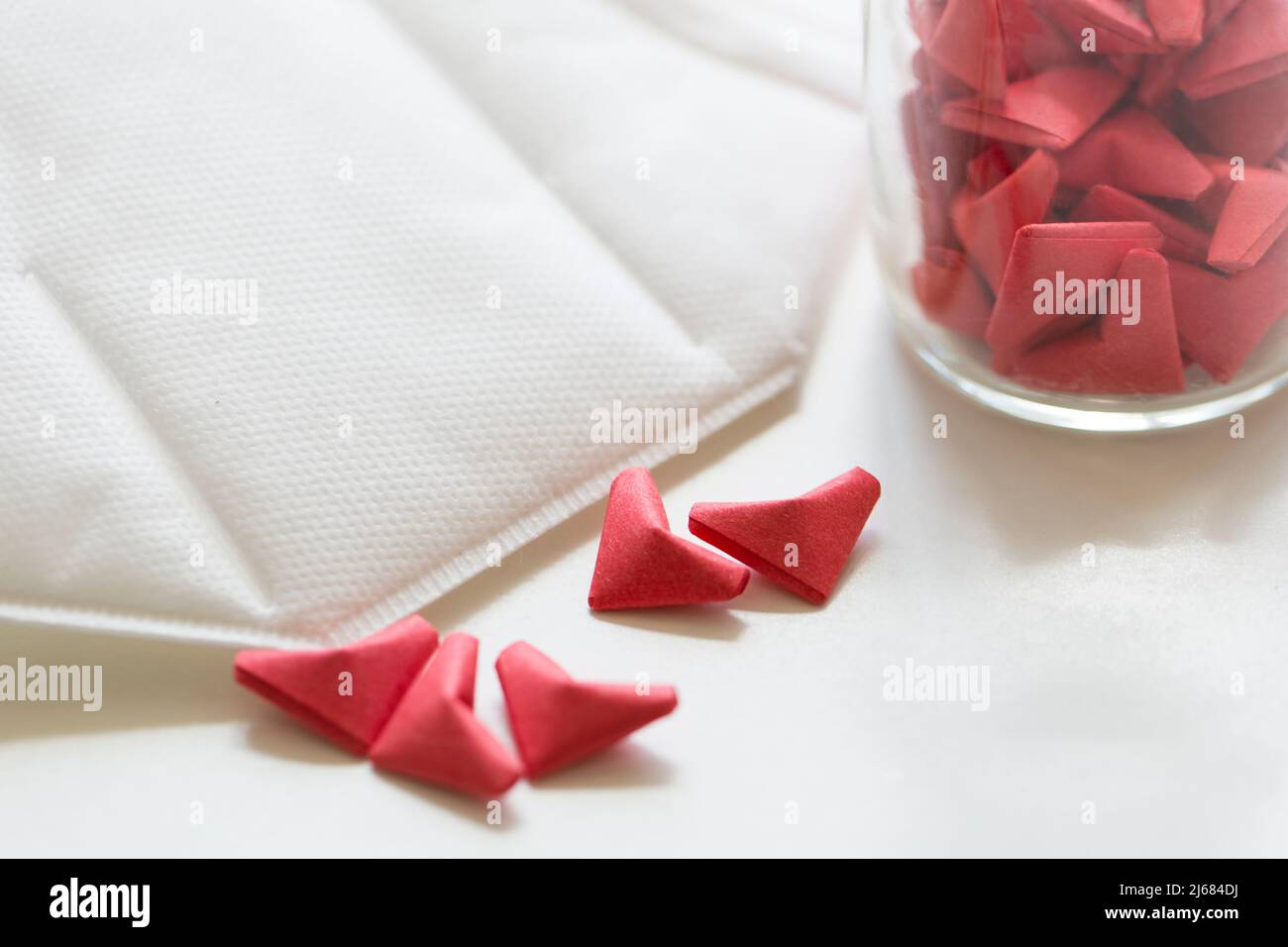 White facemask, Pink and red three-dimensional origami artwork and transparent glass jar - stock photo Stock Photo