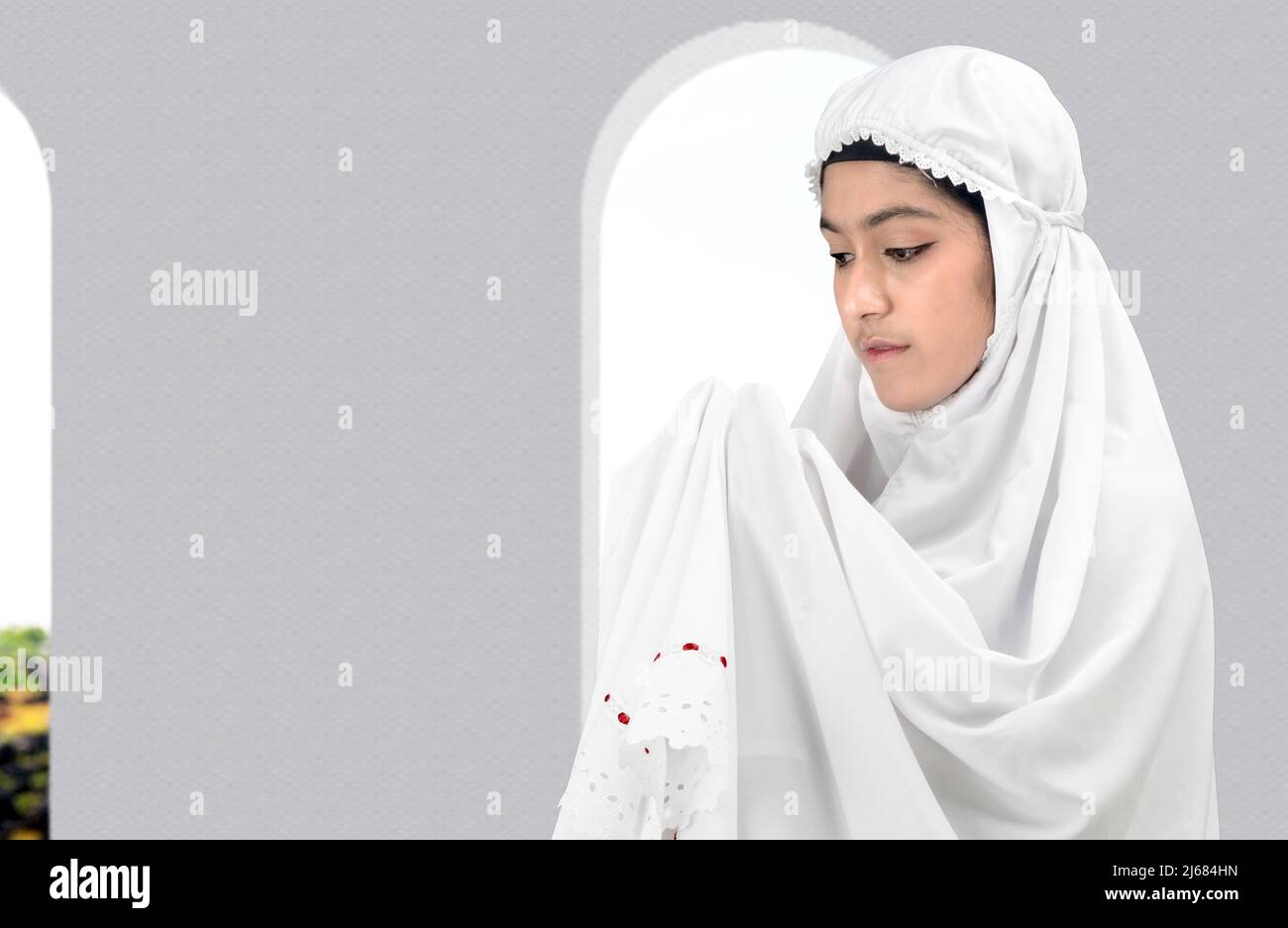 Asian Muslim woman in a veil standing while raised hands and praying on ...