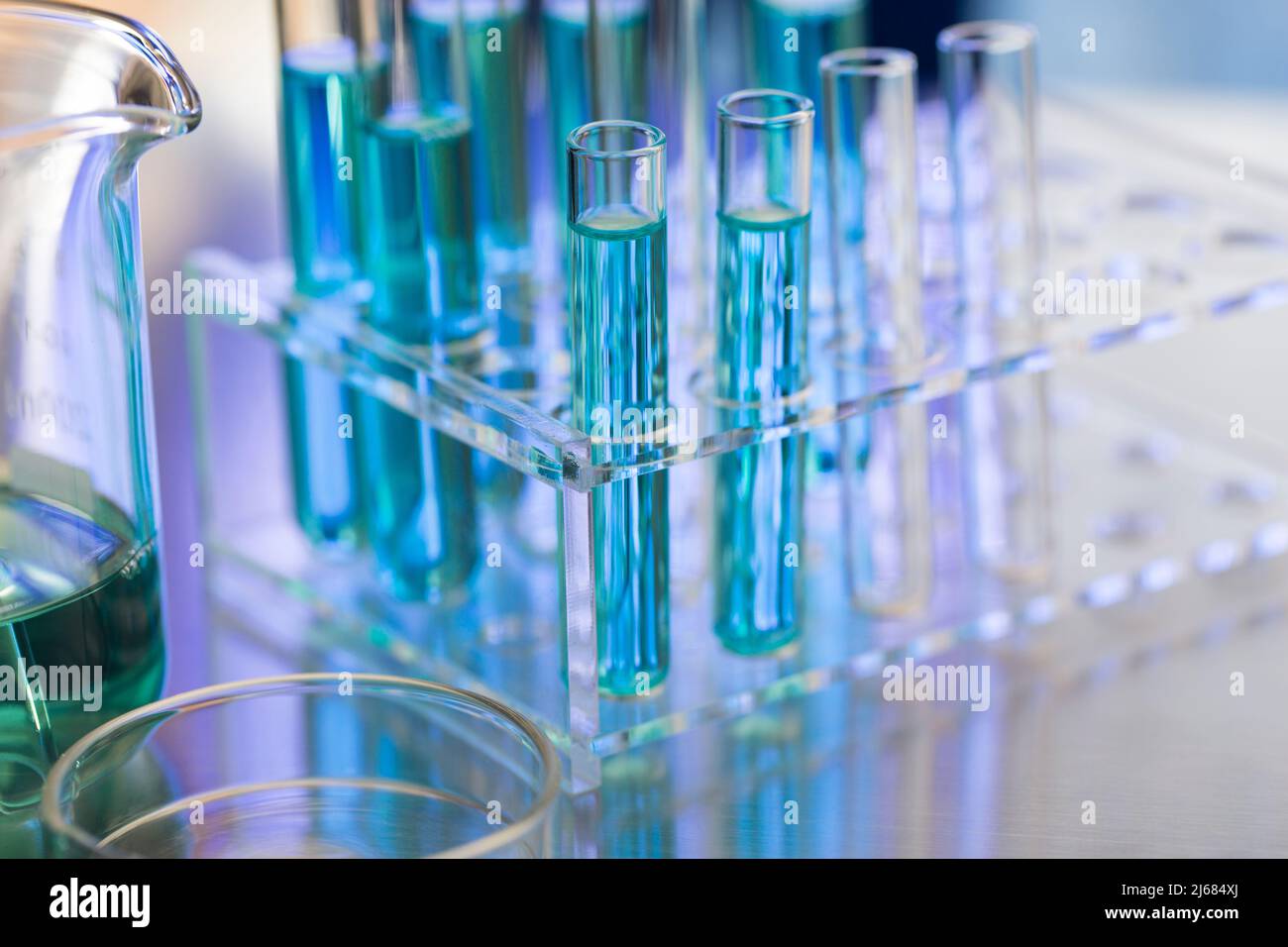 Neatly arranged test tubes containing blue reagent in chemistry laboratory with beaker and petri dishe - stock photo Stock Photo