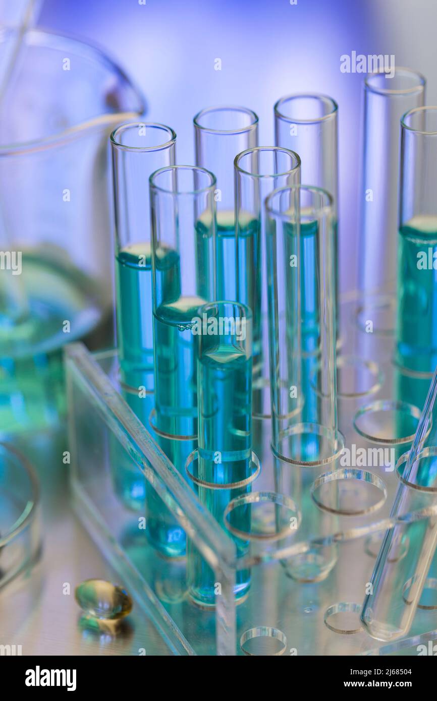 Neatly arranged test tubes containing blue reagent in chemistry laboratory with beaker and soft capsule - stock photo Stock Photo