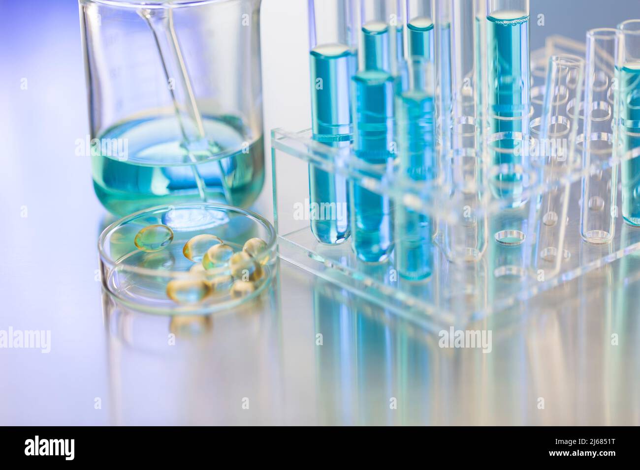 Glass dish containing soft capsules in a chemistry LABS with beaker and test tube rack  - stock photo Stock Photo