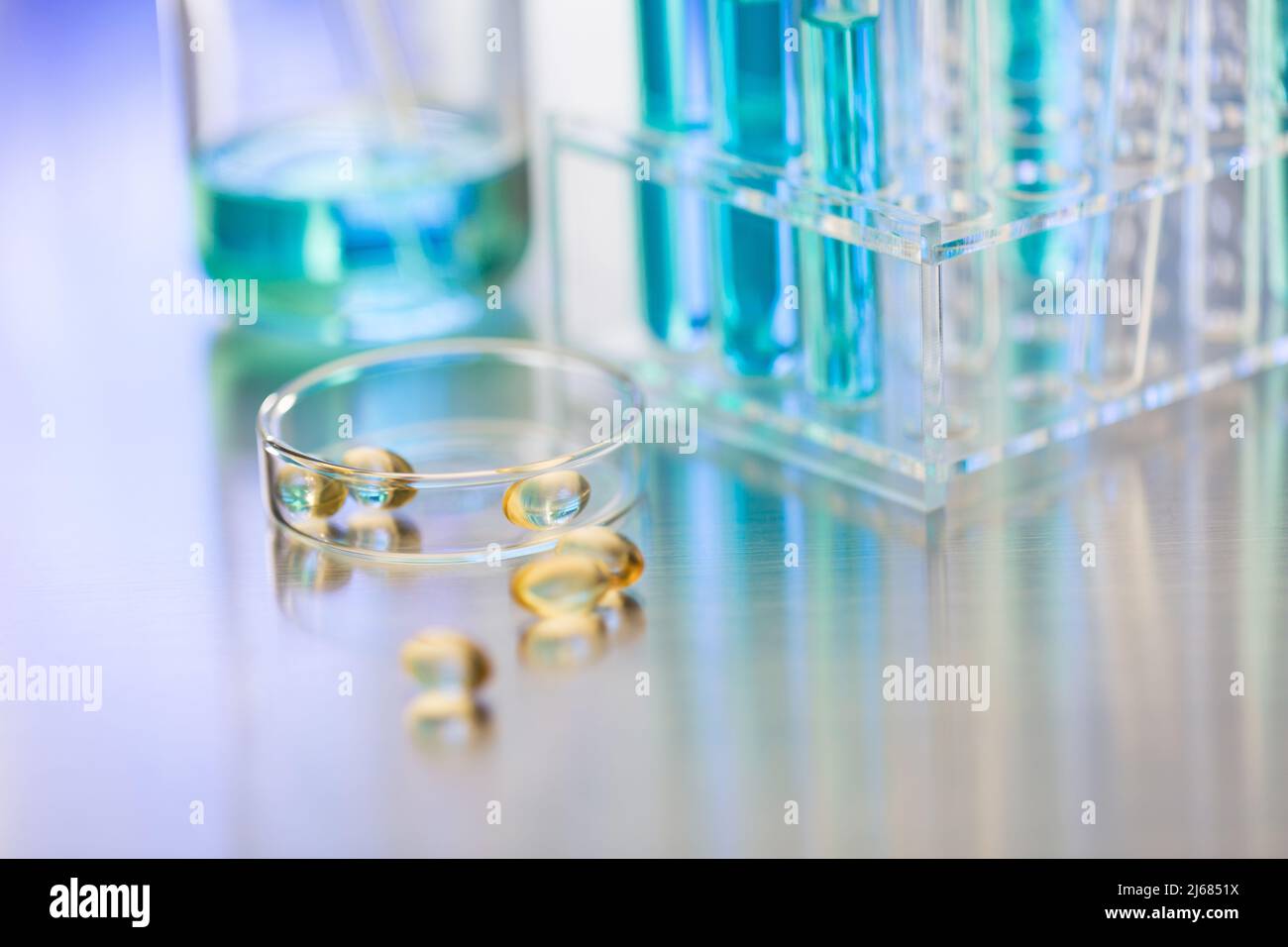 Glass dish containing soft capsules in a chemistry LABS with beaker and test tube rack - stock photo Stock Photo