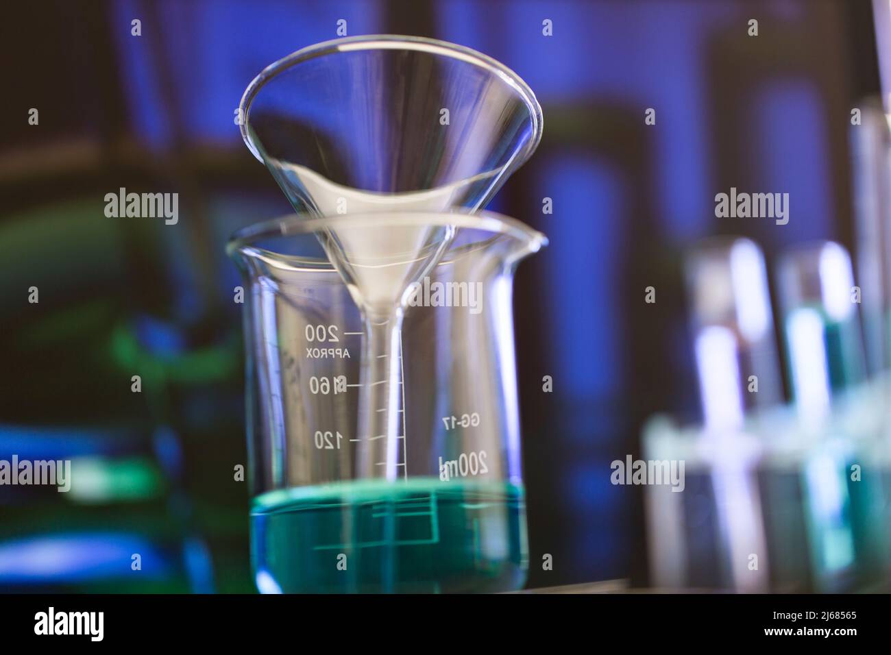 Crystal clear glass funnel in a beaker filled with blue chemical reagent - stock photo Stock Photo