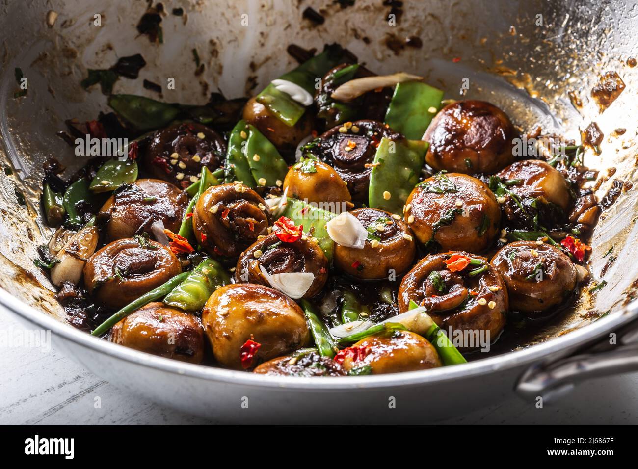 Roasted mushrooms in a wok with spring peas, onion and teriyaky sauce. Stock Photo