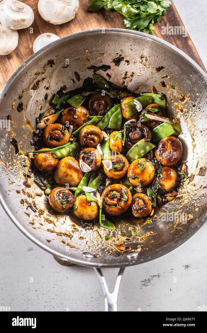 Roasted mushrooms in a wok with spring peas, onion and teriyaky sauce - Top of view. Stock Photo