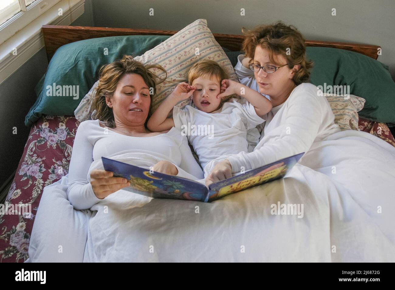 A family with two moms enjoys a morning bed together Stock Photo