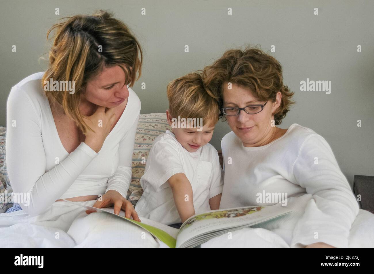 A family with two moms enjoys a morning bed together Stock Photo