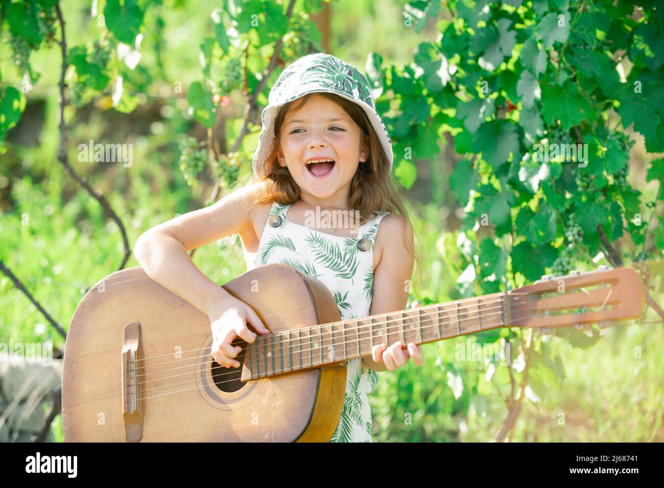 Child musician playing guitar. Stylish little child girl wearing a summer  dress having fun on backyard. Dreamy kids face Stock Photo - Alamy