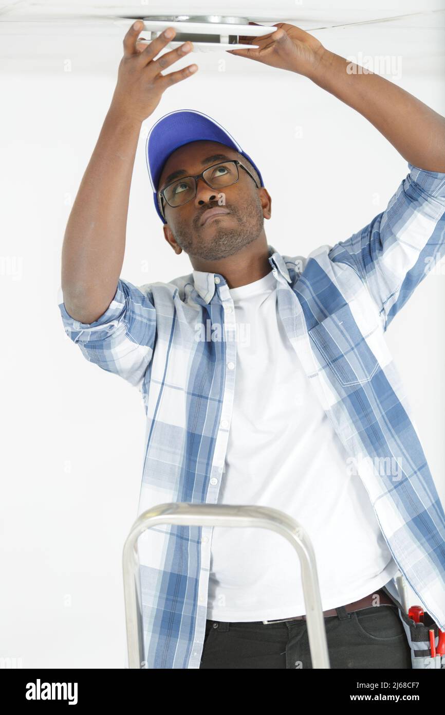 male worker using ladder installs smoke detector Stock Photo