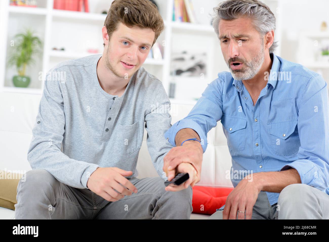 Boy changing channel on television, man objecting Stock Photo - Alamy