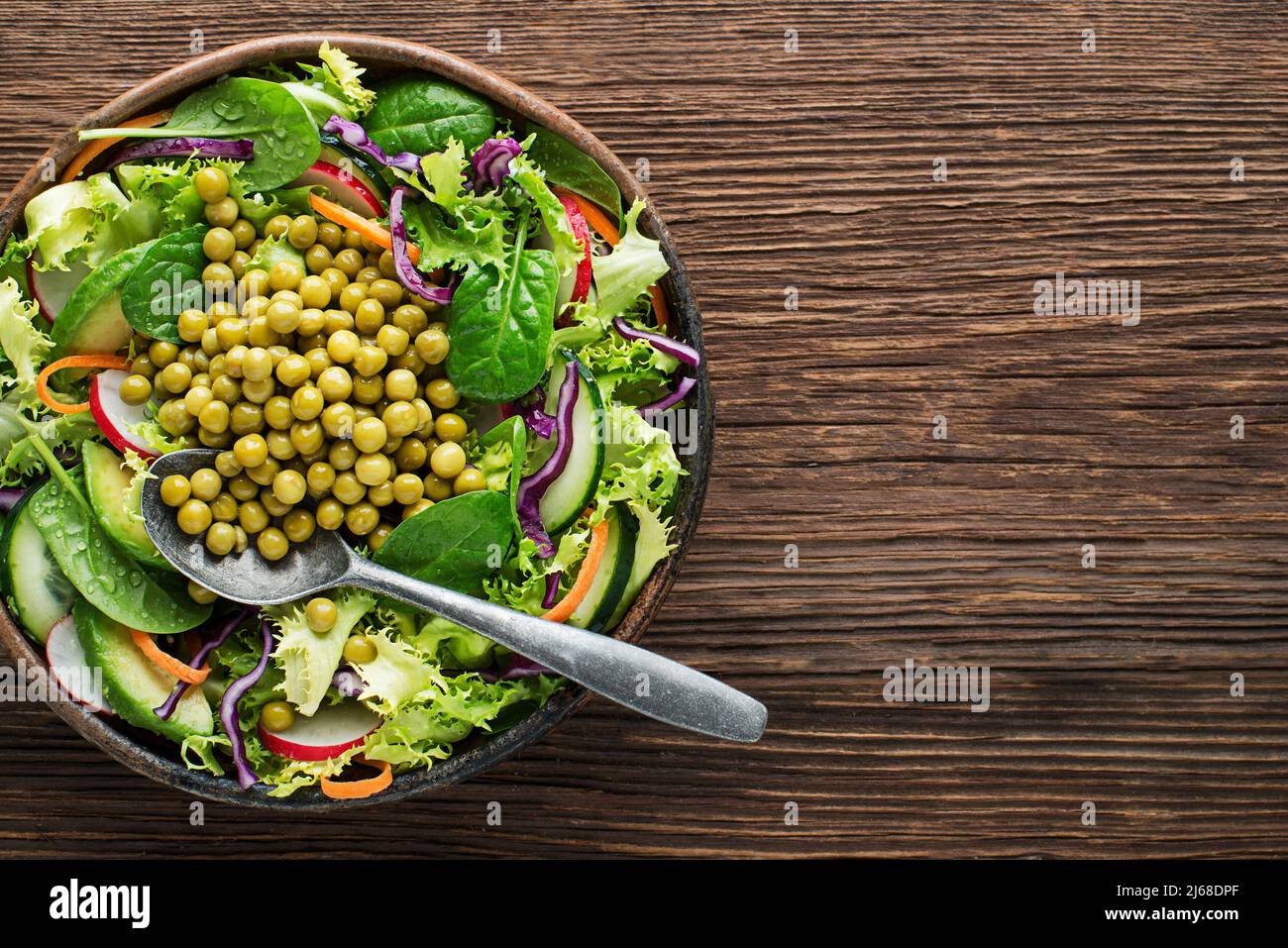 Green lettuce salad meal with fresh vegetables and cooked peas on wooden table background Stock Photo