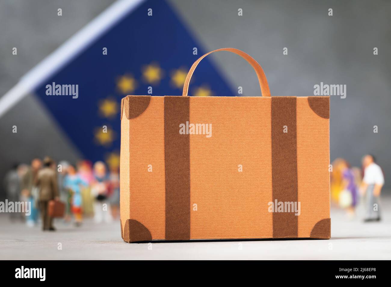 Cardboard suitcase, plastic toy people and a flag on an abstract background, a concept on the theme of moving or migration to the European Union Stock Photo