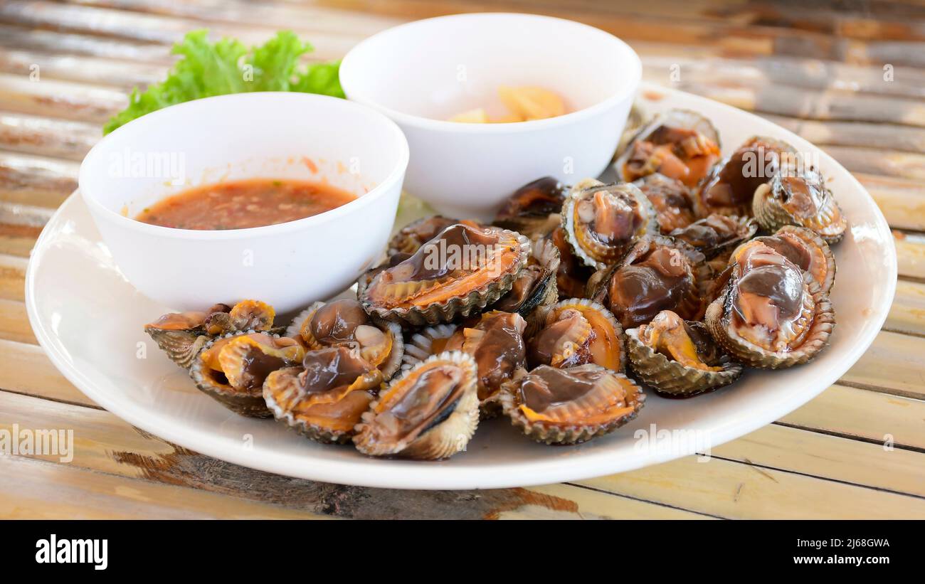 Parboiled cockles or bloody cockles with spicy Thai style dip sauce and garlic on bamboo table background. Stock Photo