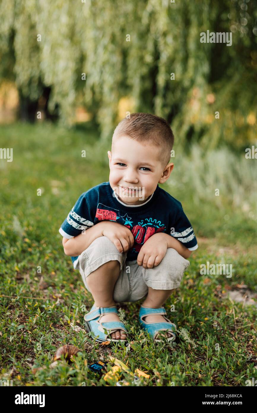 Little boy sits in the grass and smiles sweetly Stock Photo