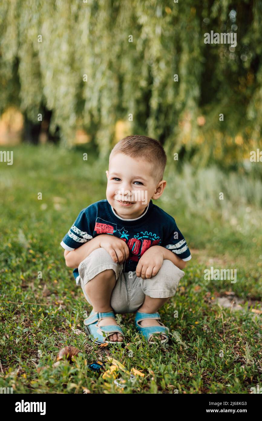 Little boy sits in the grass and smiles sweetly Stock Photo