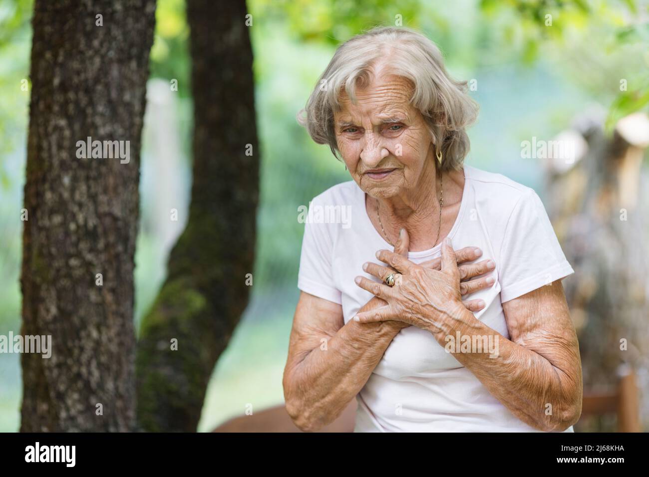 Elderly woman outdoors with heart pain holding her chest Stock Photo
