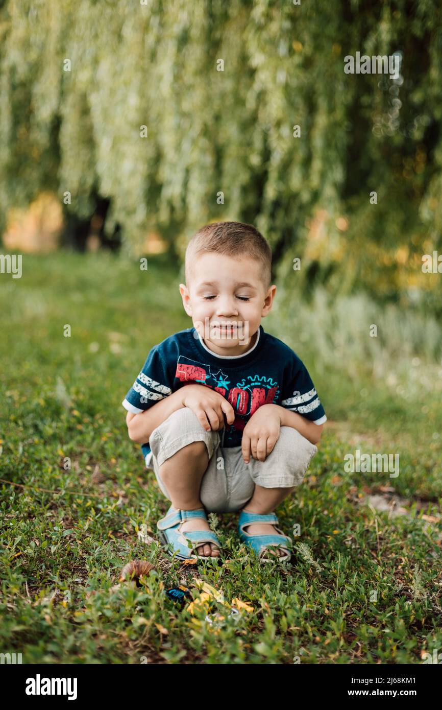 A small child crouched in the grass, closed his eyes and smiled Stock Photo