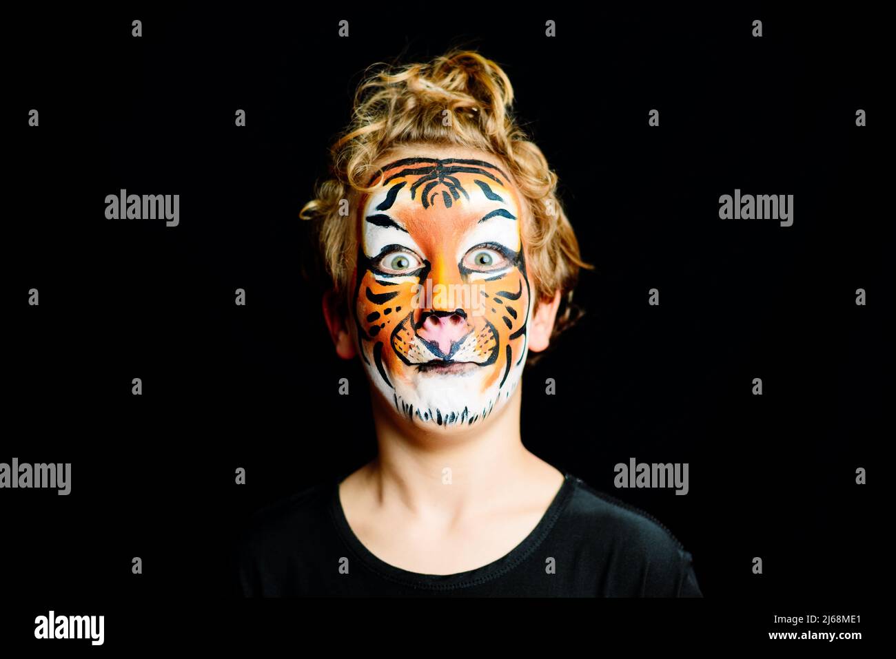 Portrait of a boy with strange and scary gesture, made up with tiger face, isolated on black background. Stock Photo
