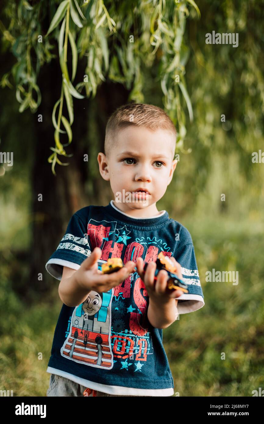 A little boy holds a toy in his hands and plays in nature under a tree Stock Photo