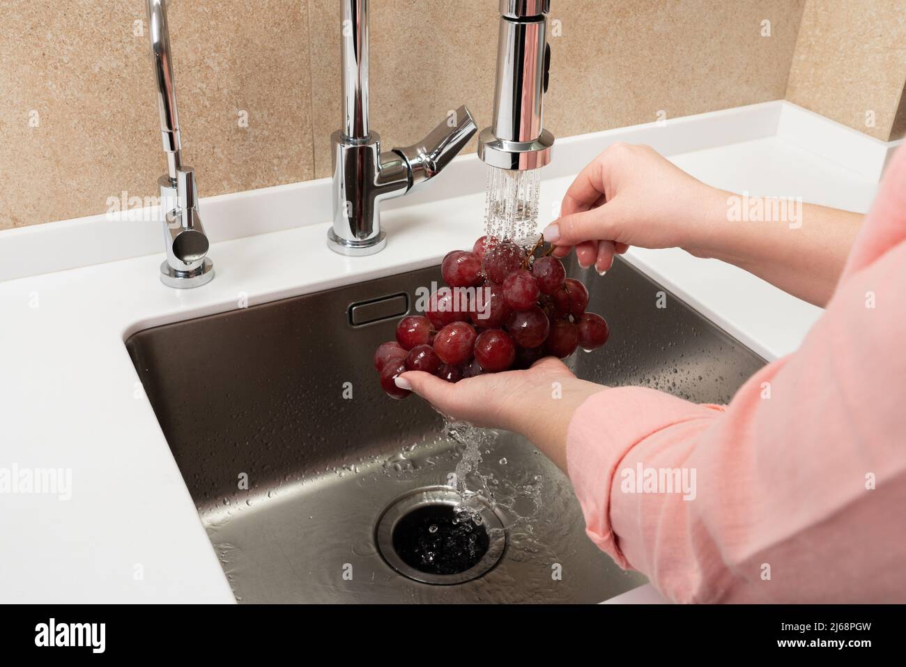 Female hands wash black grapes under the tap. Cook woman washes a bunch