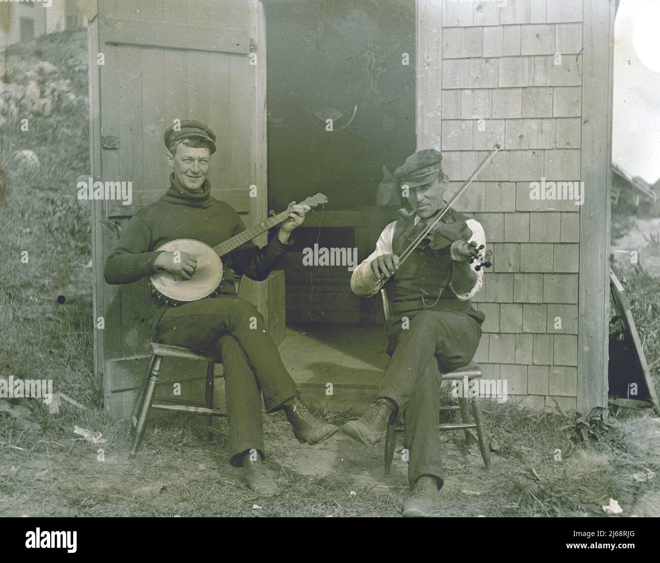 Two men, seated outside a shanty in Codfish Park, one is playing the banjo, and the other the fiddle, Sconset Gully, Cary's Fish House, Nantucket, USA Stock Photo