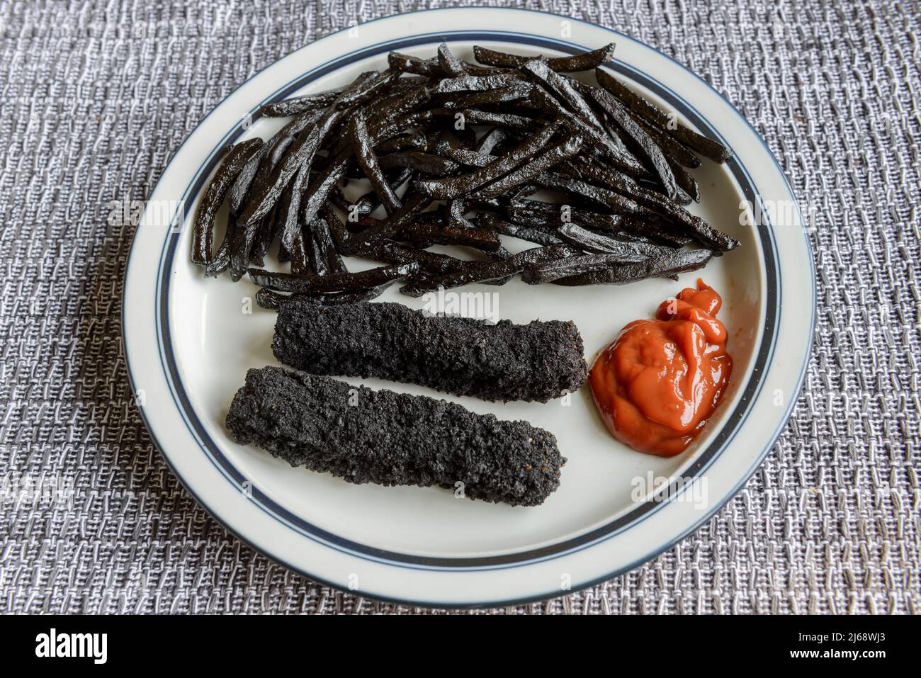 A plate of badly burnt, black, fish fingers and chips, French fries. Stock Photo