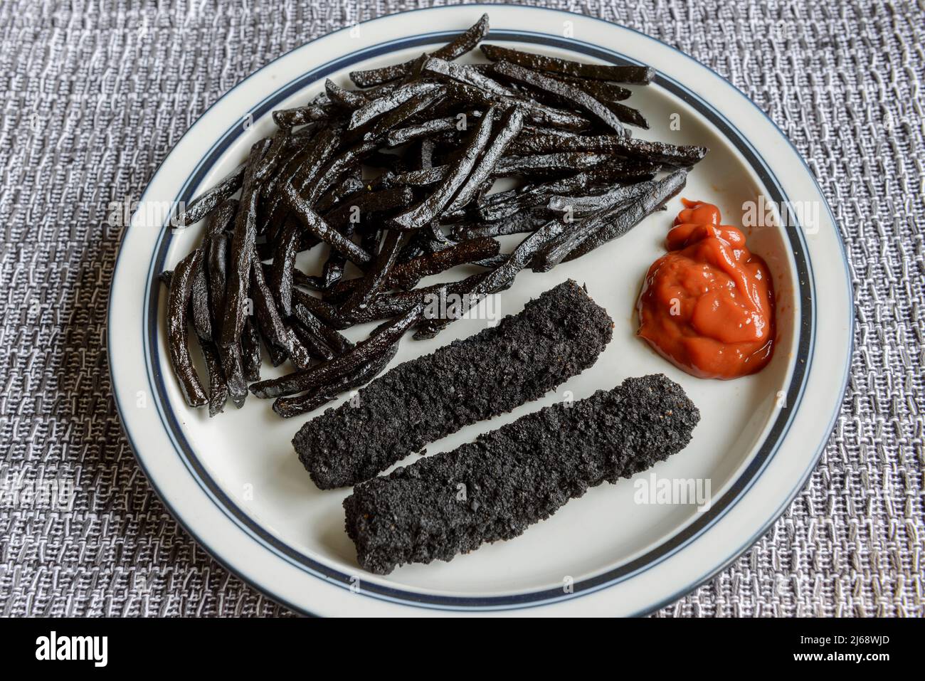 A plate of badly burnt, black, fish fingers and chips, French fries. Stock Photo