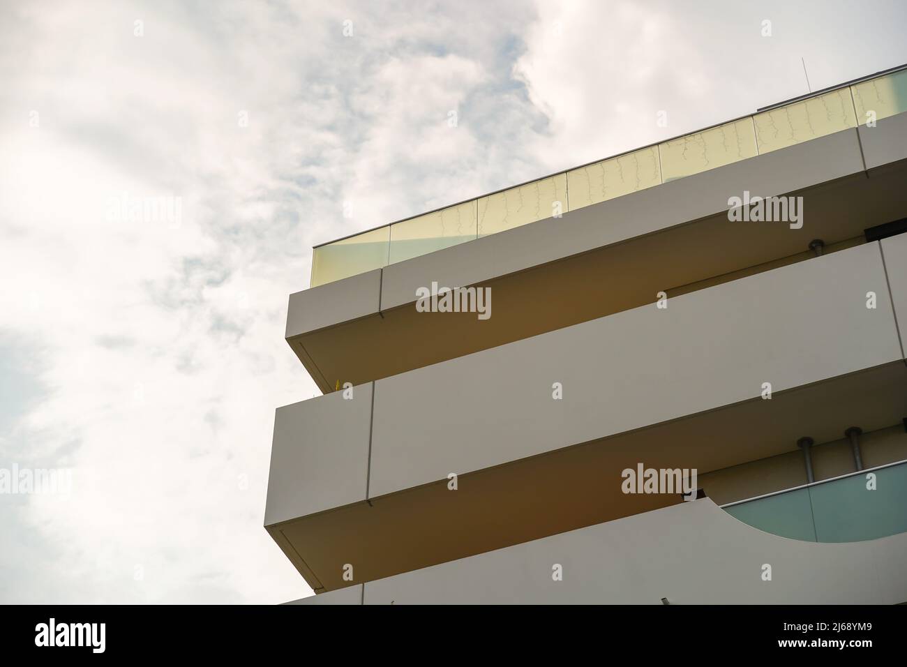 Facade and balcony of a tall building in the city. Glass of the railings of the rooftop terrace is in front of the sky. Small clouds in the sky. Stock Photo