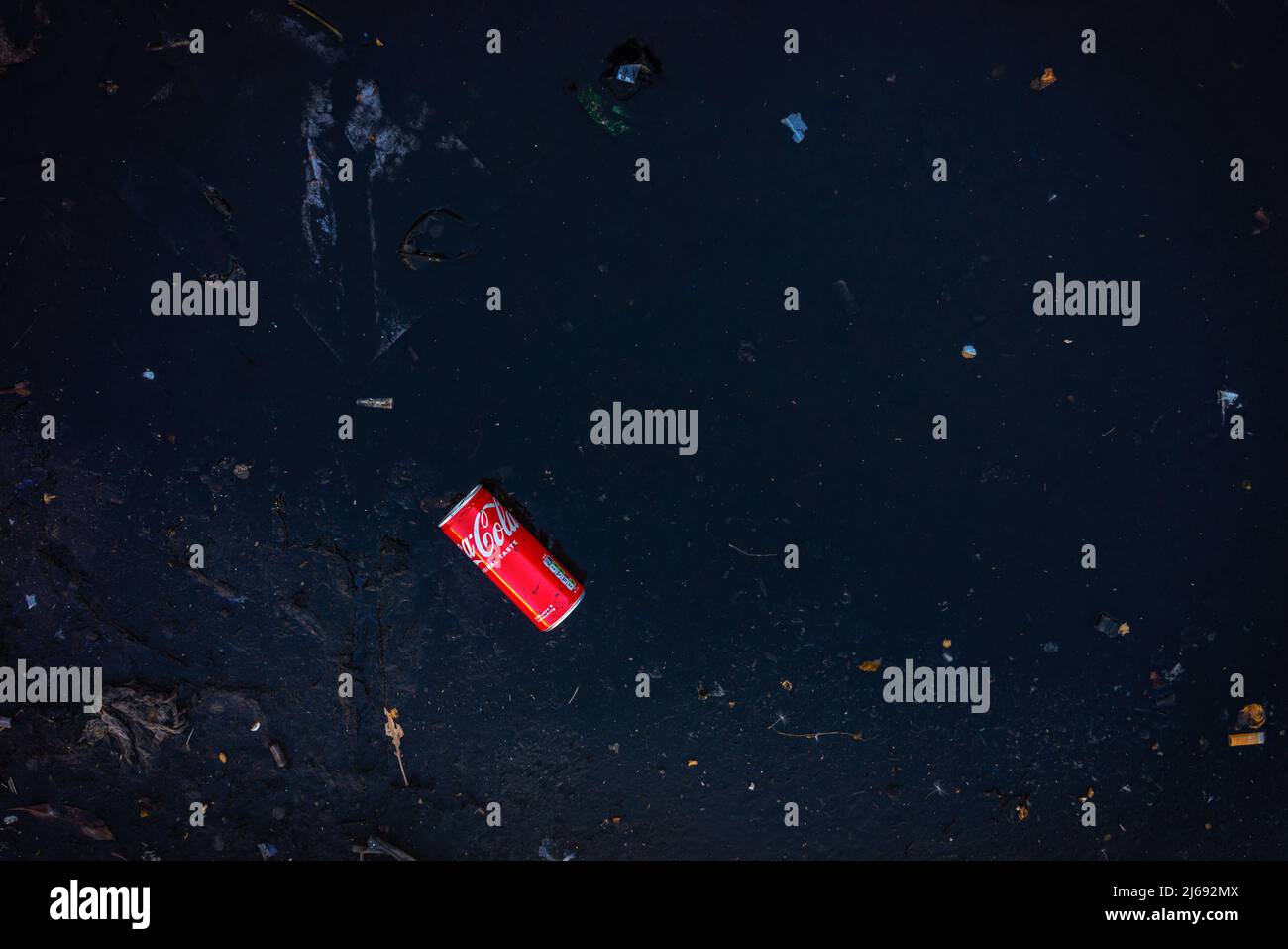 Discarded can of Coca-Cola (coke) amongst other rubbish in a puddle Stock Photo
