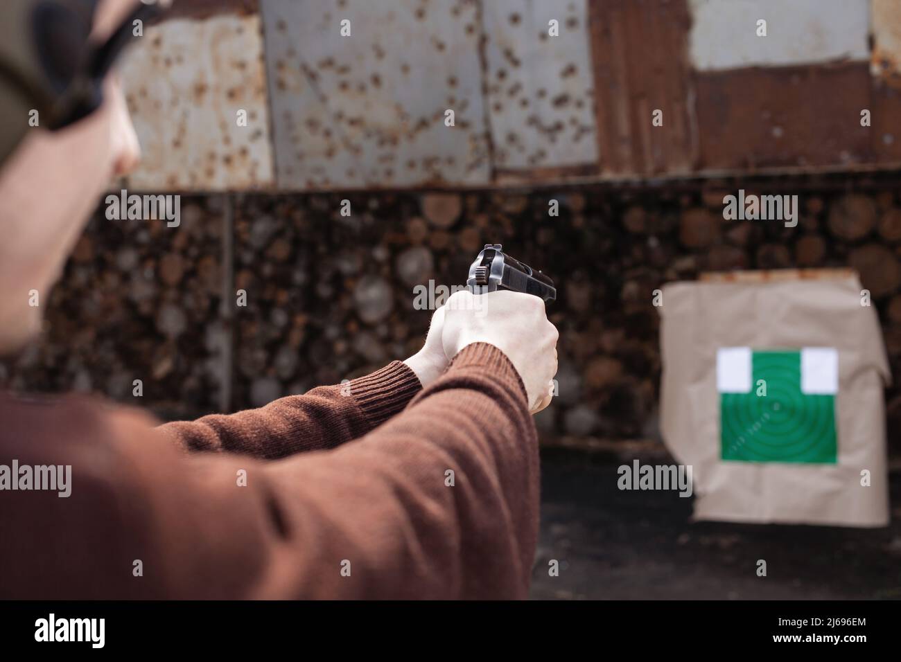 A young man shoots a gun, aiming at the target. A man wearing