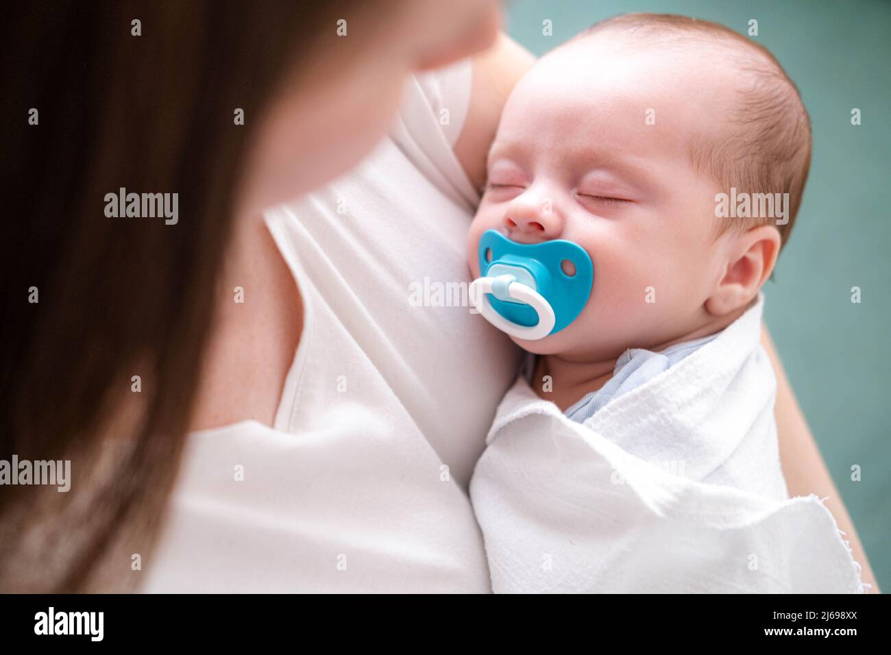 Little newborn baby boy sleeping with baby dummy on mother hands at