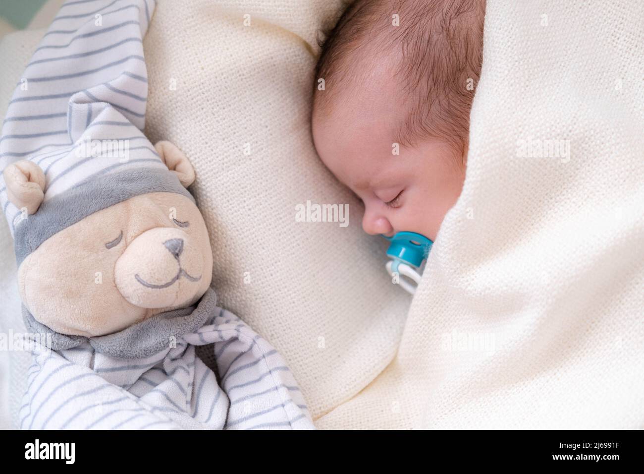 Little newborn baby boy sleeping in crib with baby dummy and teddy bear