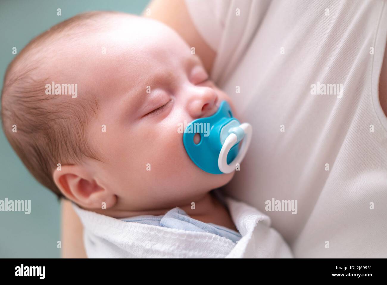 Little newborn baby boy sleeping with baby dummy on mother hands at