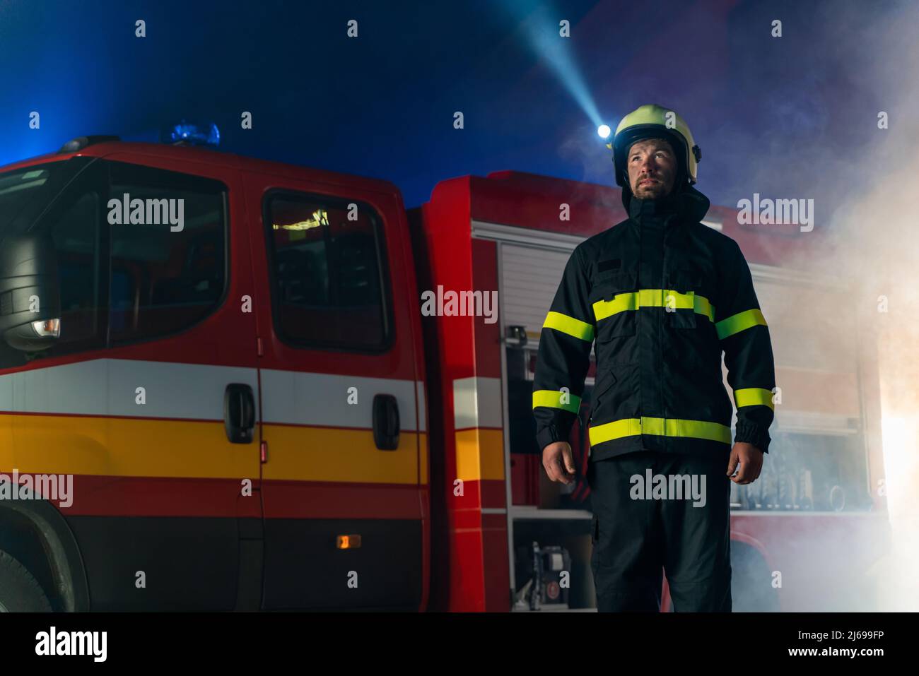 Low angle view of firefighter with fire truck in background at night. Stock Photo