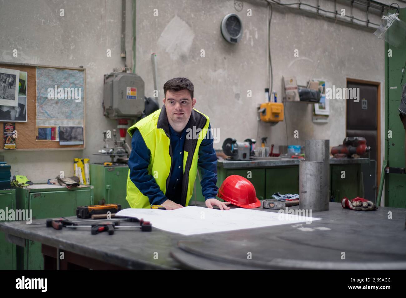 Young man with Down syndrome looking at blueprints when working in industrial factory, social integration concept. Stock Photo
