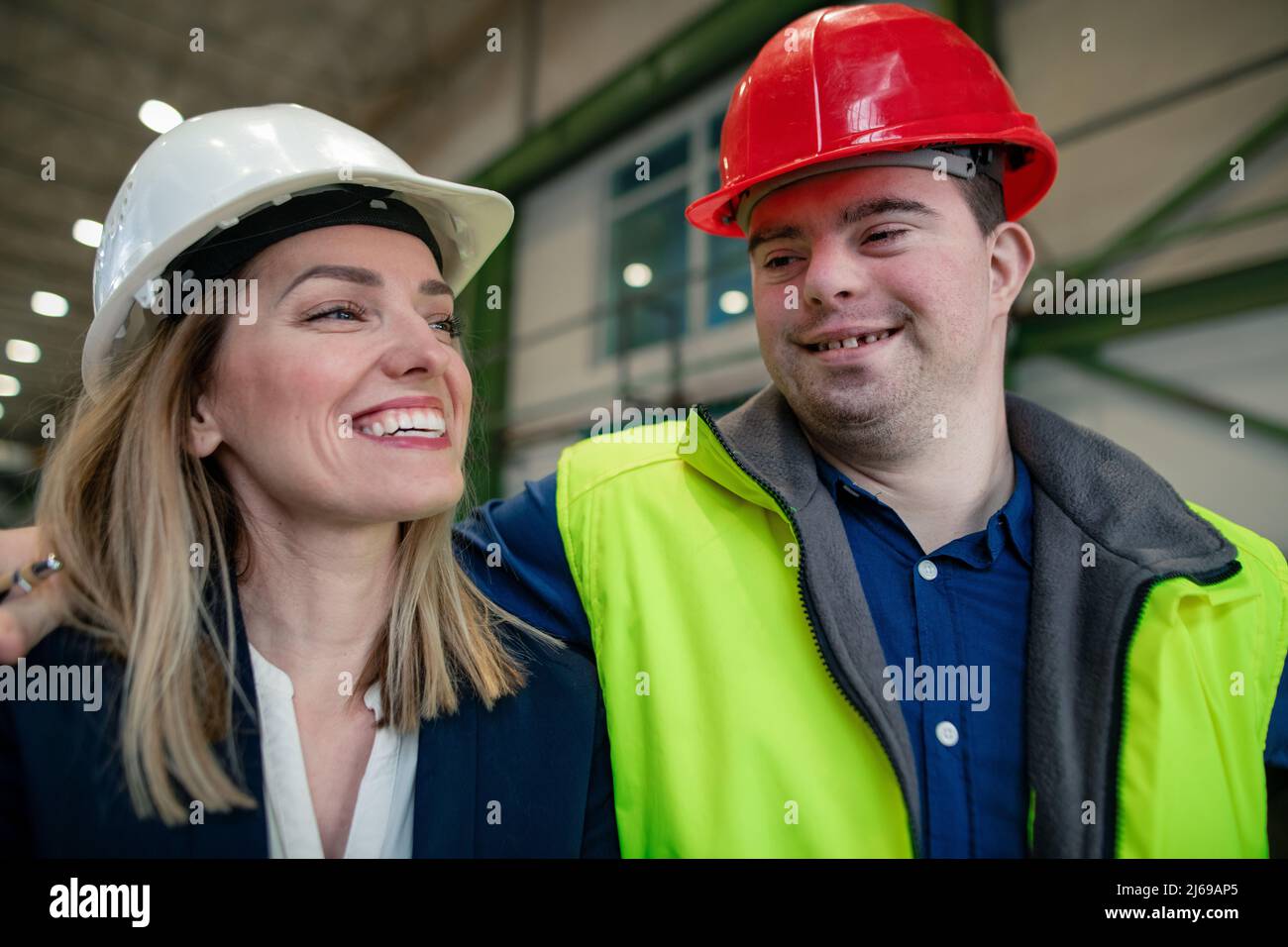 Young man worker with Down syndrome with manager working in industrial factory, social integration concept. Stock Photo