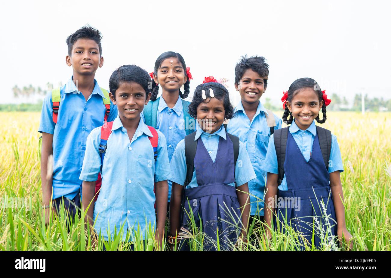 group of happy smiling village school kids in uniform standing at middle paddy field by looking camera - concept of friendship, education and Stock Photo