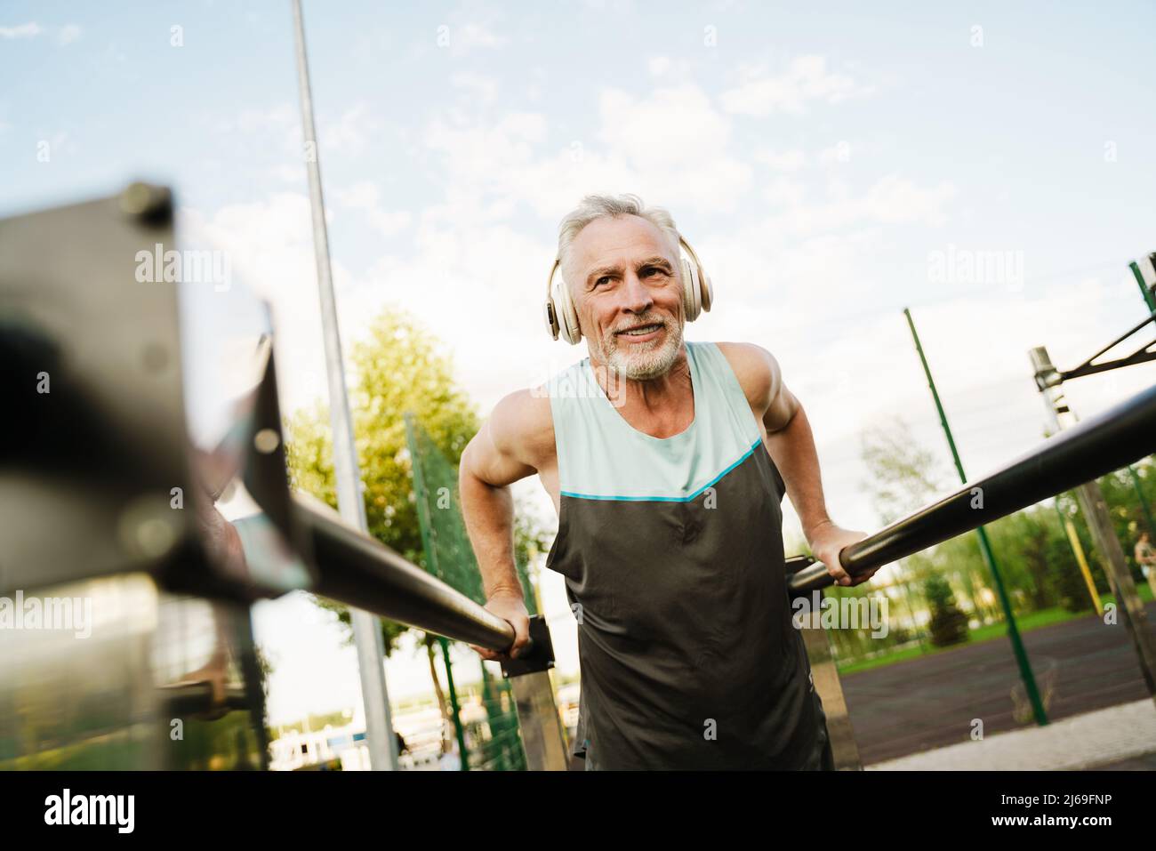 Grey senior sportsman listening music while working out on parallel