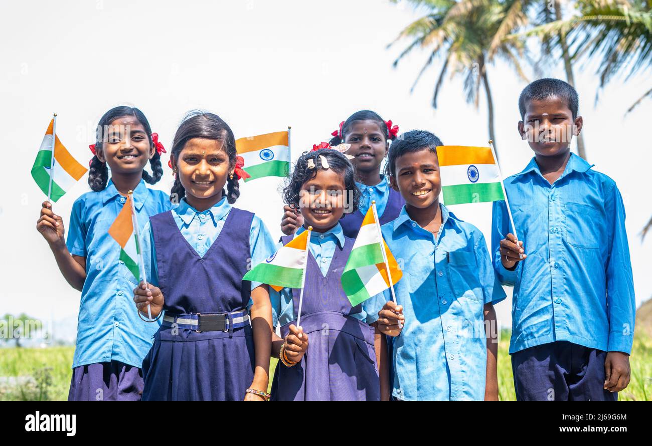 group of happy smiling village school kids in unifrom holding Infian flag by looking at camera during independence day celebrations - conept of Stock Photo