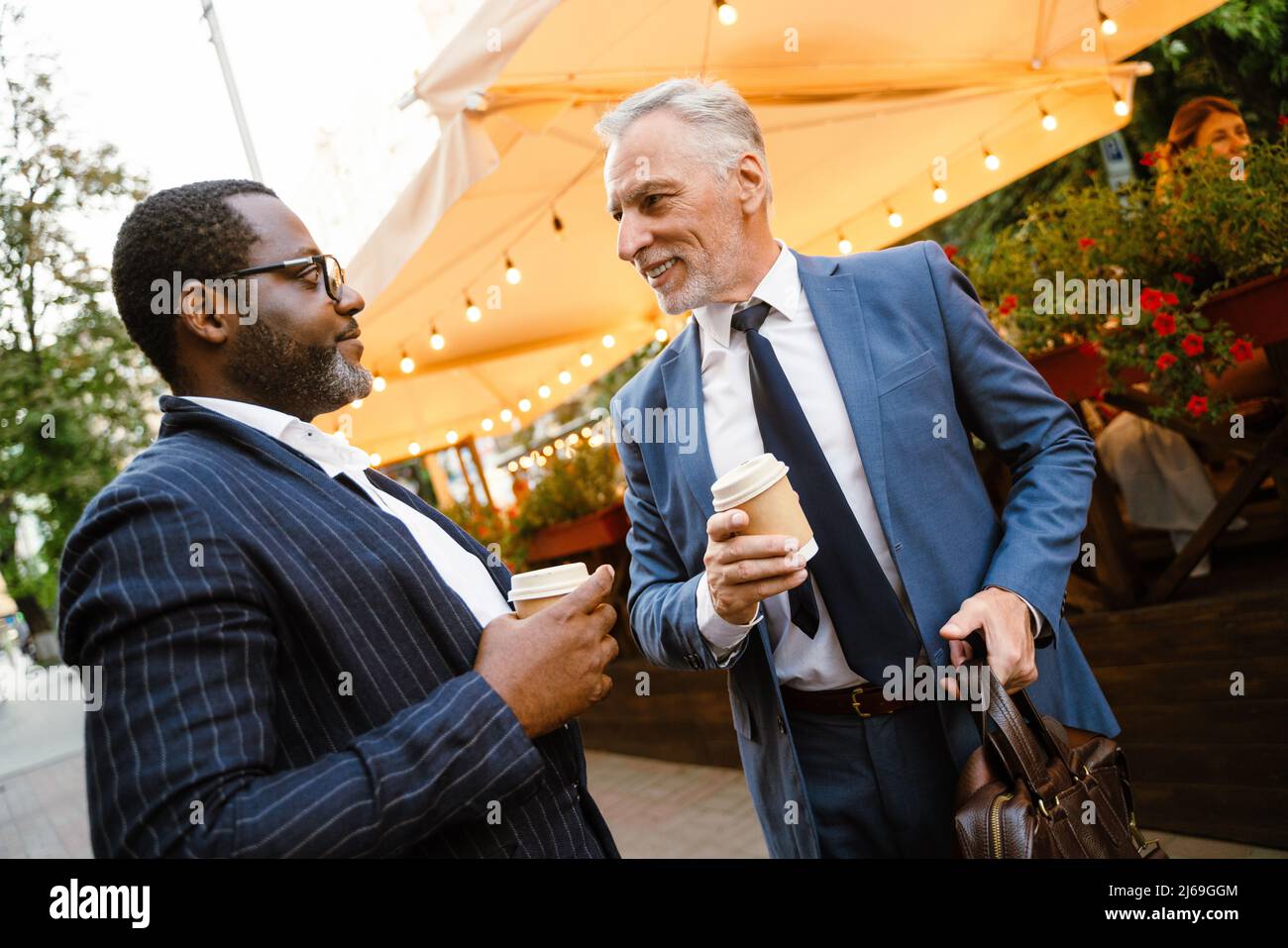 Multiracial two men wearing suits talking while drinking coffee outdoors Stock Photo