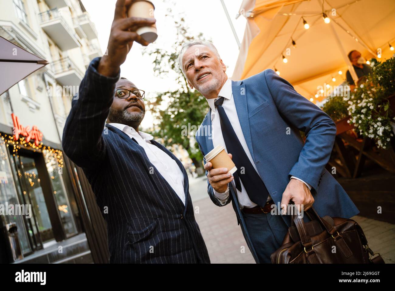 Multiracial two men wearing suits talking while drinking coffee outdoors Stock Photo
