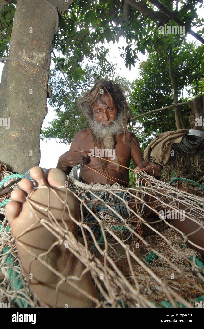 Narayanganj, Bangladesh - June 07, 2007: A fisherman is sewing his net while sitting on the bank of Meghna River at Narayanganj in Bangladesh. Stock Photo