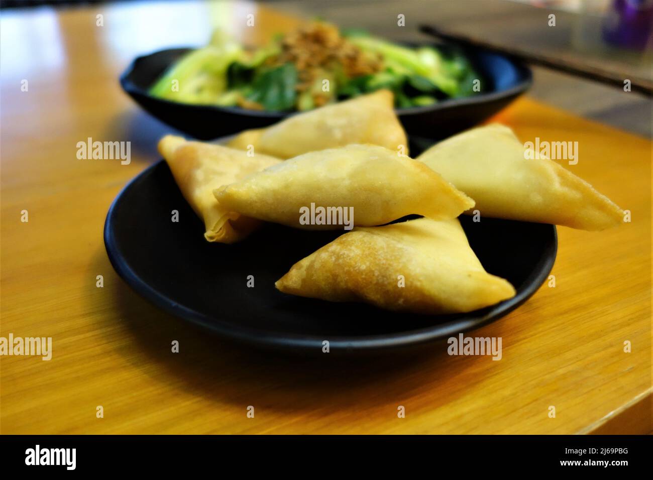 Samosas on a black plate as a close up with green vegetables in the background Stock Photo